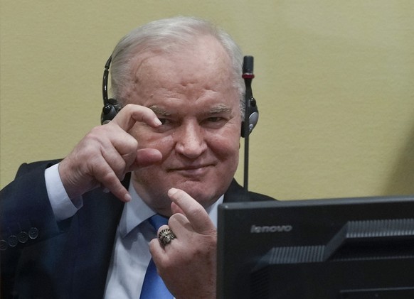 Former Bosnian Serb military chief Ratko Mladic imitates taking pictures as he sits the court room in The Hague, Netherlands, Tuesday, June 8, 2021, where the United Nations court delivers its verdict ...