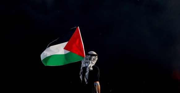 epa09984902 A Palestinian waves Palestine flag during clashes with Israeli troops near Huwwara checkpoint in the West Bank city of Nablus, 29 May 2022. According to Palestinian medical sources, 70 Pal ...
