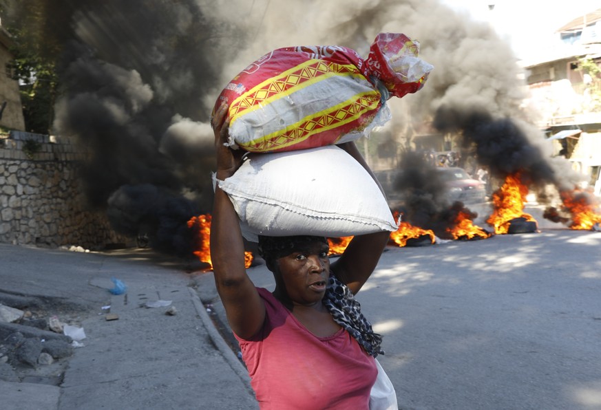 A woman walks past burning tires set on fire by protesters to call attention to the country&#039;s insecurity and demanding the resignation of the prime minister, in Port-au-Prince, Haiti, Thursday, J ...