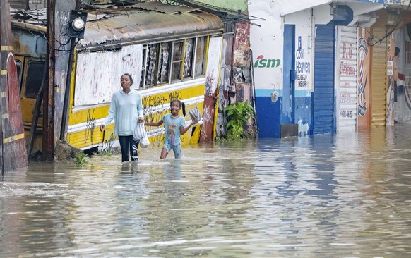 People walk through a street flooded by the rains of Tropical Storm Franklin in Santo Domingo, Dominican Republic, Tuesday, Aug. 22, 2023. (AP Photo/Ricardo Hernandez)