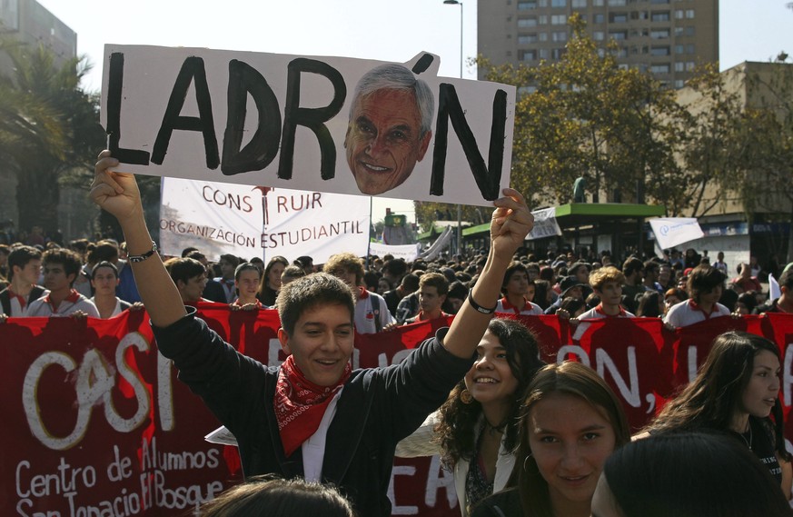 A student holds a banner with the image of President Sebastian Piñera and the word thief written in Spanish, during a protest in Santiago, Chile, on Thursday, April 19, 2018. Thousands of people march ...