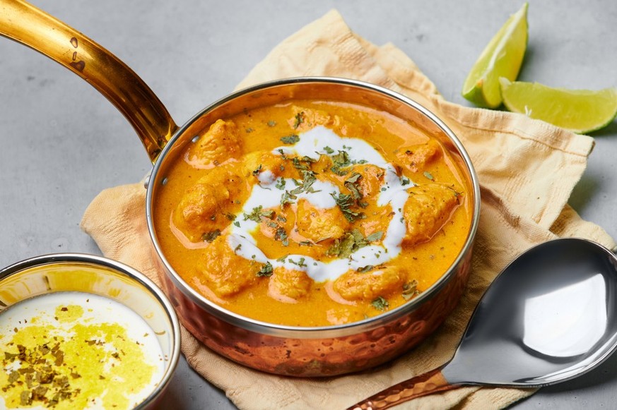 Murgh Makhani or Butter Chicken in copper bowl on gray concrete table top. Indian Cuisine dish with chicken meat and creamy masala. Asian food and meal.