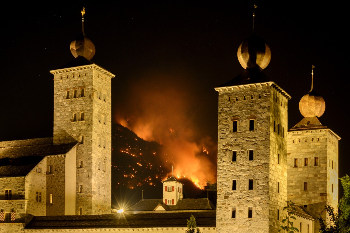 De la fumee et des flammes s'echappent de la foret en feu au dessus des communes de Bitsch et Ried-Moerel ce lundi 17 juillet 2023 derriere le chateau Stockalper a Brig. Un incendie de foret s  ...