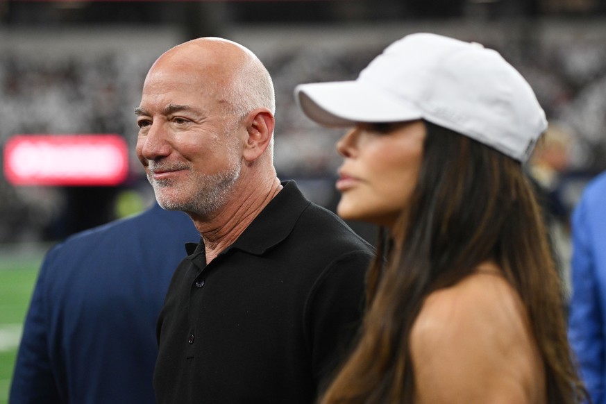 Jeff Bezos, left, stands on the field with his wife Lauren Sanchez Bezos prior to an NFL football game between the Dallas Cowboys and the Washington Commanders in Arlington, Texas, Sunday, Sept. 20, 2 ...