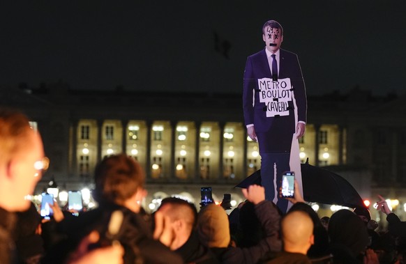 Demonstrators hold a placard depicting French President Emmanuel Macron that reads, &quot;metro, work, grave&quot; during a protest in Paris, Friday, March 17, 2023. Protests against French President  ...
