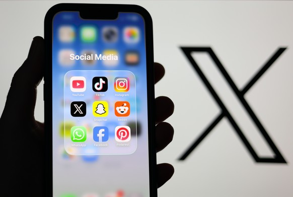 epa12674704 Social Media applications displayed on a mobile phone alongside the X logo (formerly known as Twitter) displayed on a laptop screen in Liverpool, Britain, 23 January 2026. A proposal to ba ...