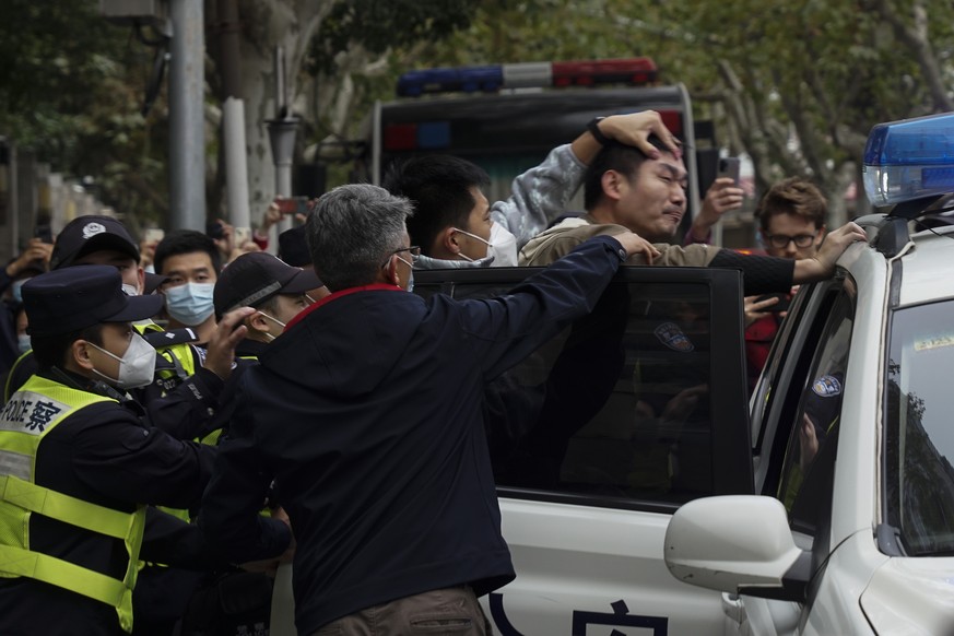 In this photo taken on Sunday, Nov. 27, 2022, a protester is forced into a police car by the police, during a protest on a street in Shanghai, China. Authorities eased anti-virus rules in scattered ar ...