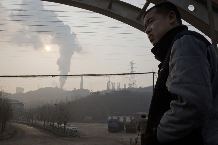 In this Dec. 30, 2016 photo, a man looks up near smoke spewing from a chimney near the Jiujiang steel and rolling mills in Qianan in northern China&#039;s Hebei province. Faced with choking smog in th ...