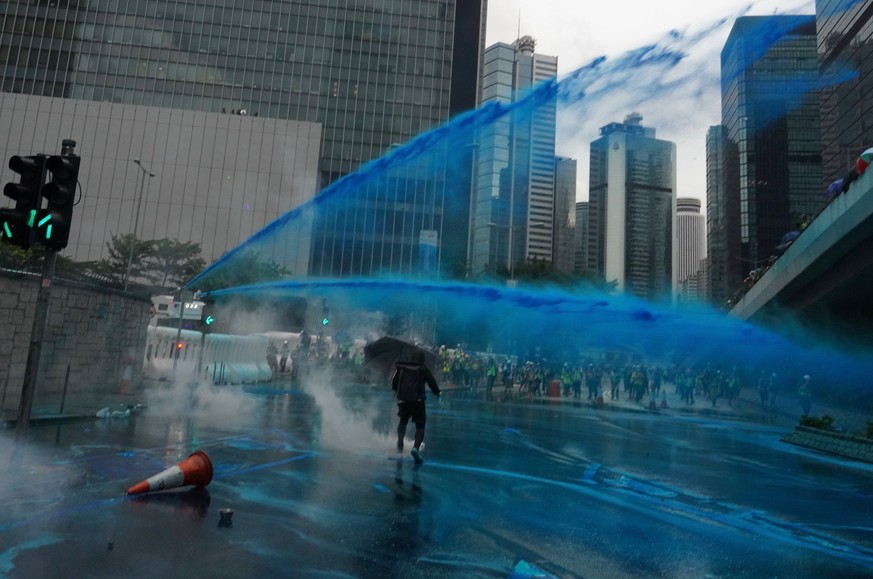 A protestor fetches an exploded tear gas shell, as blue-colored water is fired from water cannons in Hong Kong as police ready for possible confrontations near the Chinese government&#039;s main offic ...