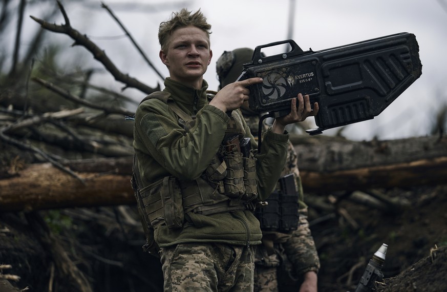 A Ukrainian soldier uses an anti-drone gun against a Russian drone as he sits in a trench near Avdiivka, in the Donetsk region, Ukraine, Friday, April 28, 2023. (AP Photo/Libkos)