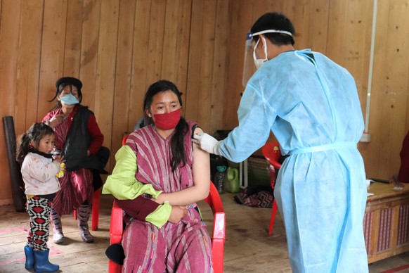 epa09367459 A handout photo made available by UNICEF Bhutan showing a young mother (C) receiving her second dose of COVID-19 vaccine at the community centre 20 July 2021 (issued 26 July 2021) in one o ...