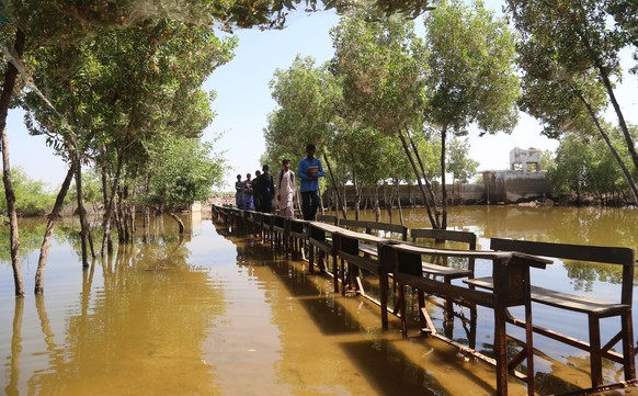 epa10234768 Students use school benches to cross floodwater at a submerged school, in Mirpur Khas district, Sindh province, Pakistan, 10 October 2022. According to disaster management authorities, aro ...
