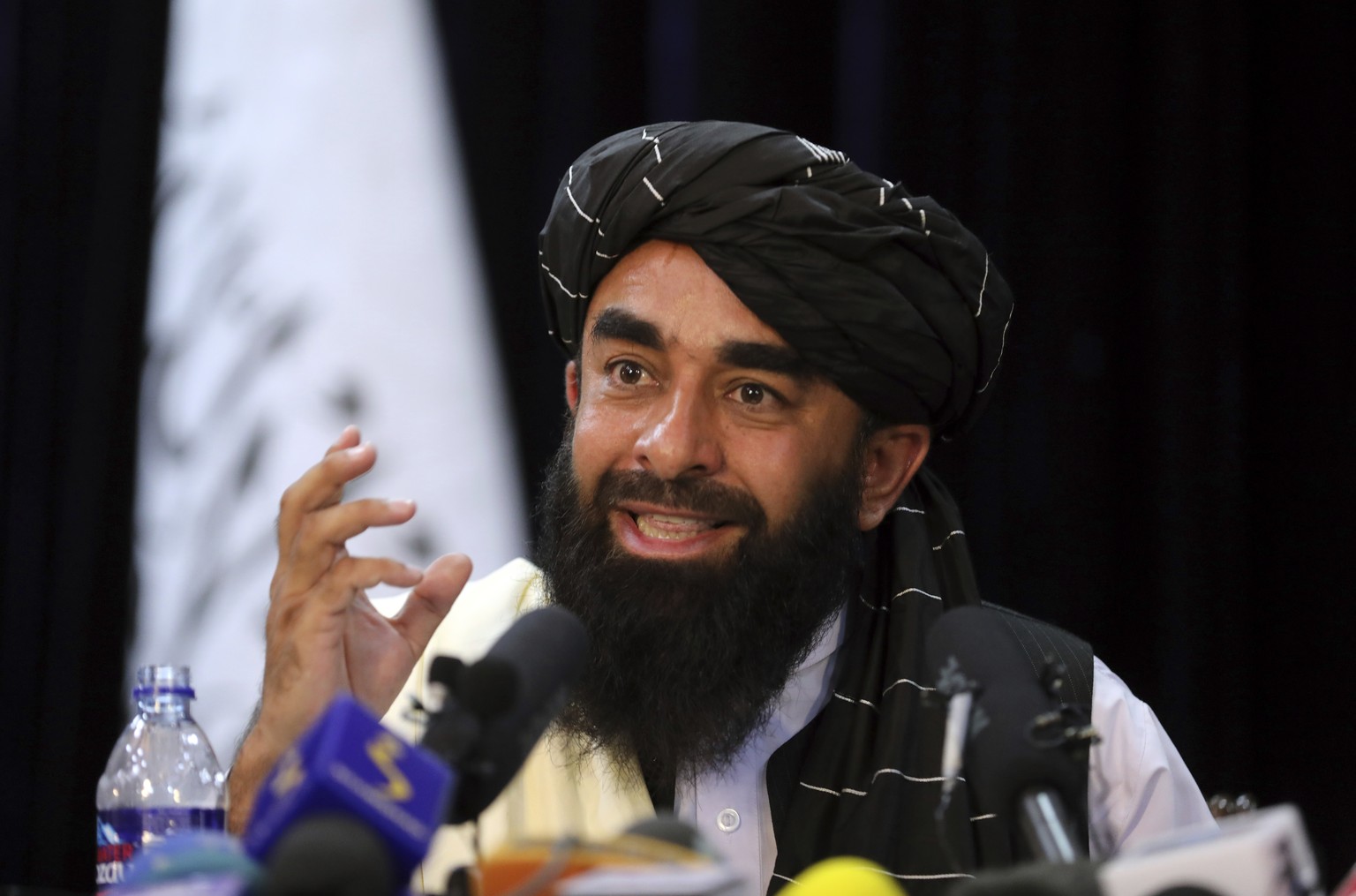 In front of a Taliban flag, Taliban spokesman Zabihullah Mujahid speaks at at his first news conference, in Kabul, Afghanistan, Tuesday, Aug. 17, 2021. For years, Mujahid had been a shadowy figure iss ...
