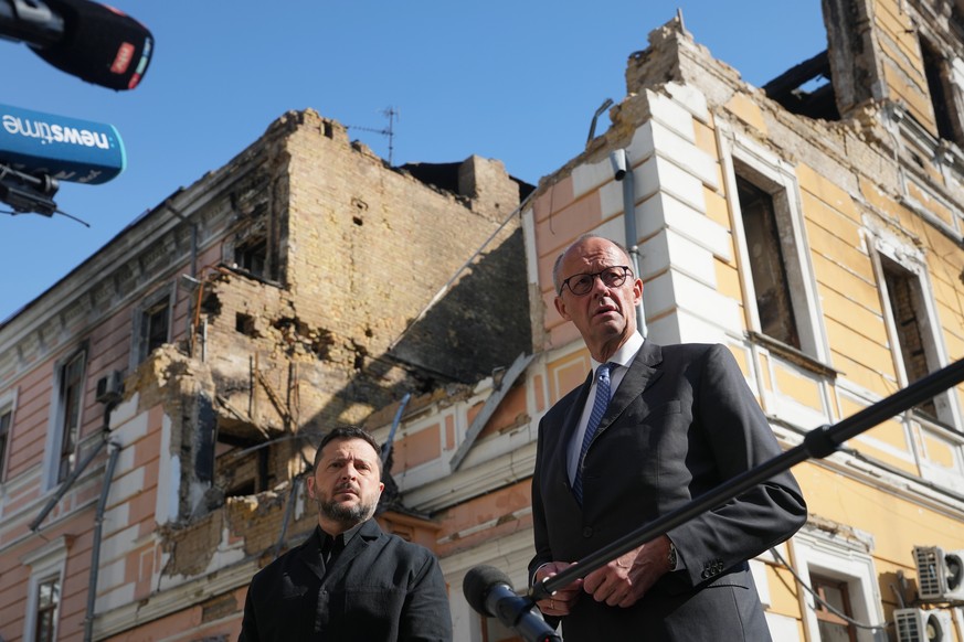 Ukraine's President Volodymyr Zelenskyy, centre, and German Chancellor Friedrich Merz speak to media with National Academy of science building damaged after a Russian drone strike, on the backgro ...