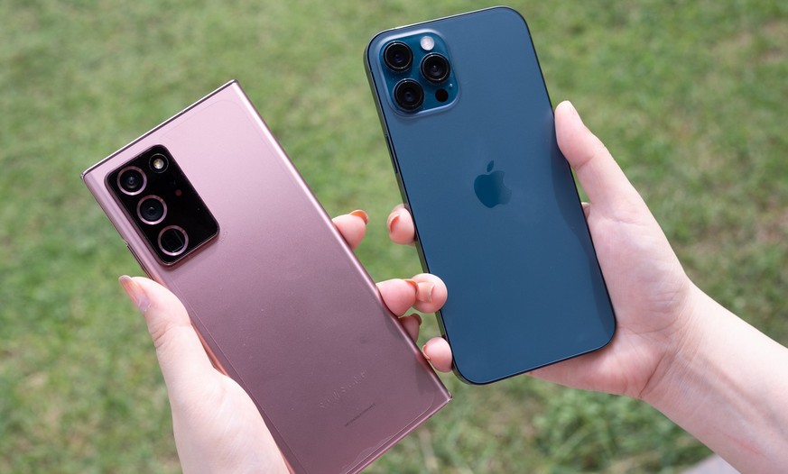 Frauenhand hält das iPhone 12 Pro Max Pacific Blue Color und das Samsung Galaxy Note 20 Ultra 5G (2020).