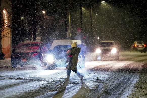 A person carries their dog as they cross Butler Street as snow falls during a winter storm that will impact the region on Sunday night, Jan. 16, 2022, in Lawrenceville a neighborhood in Pittsburgh. (A ...