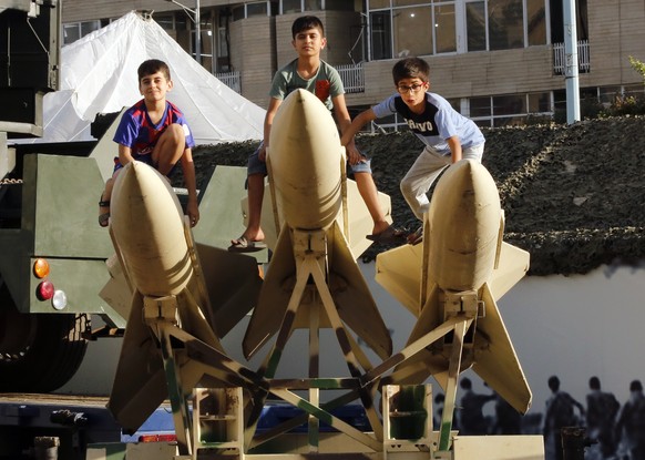 epa09487896 Iranian children sit on short-range missiles in a street exhibition by Iran's army and paramilitary Revolutionary Guard celebrating 'Defence Week' marking the 41th anniversa ...