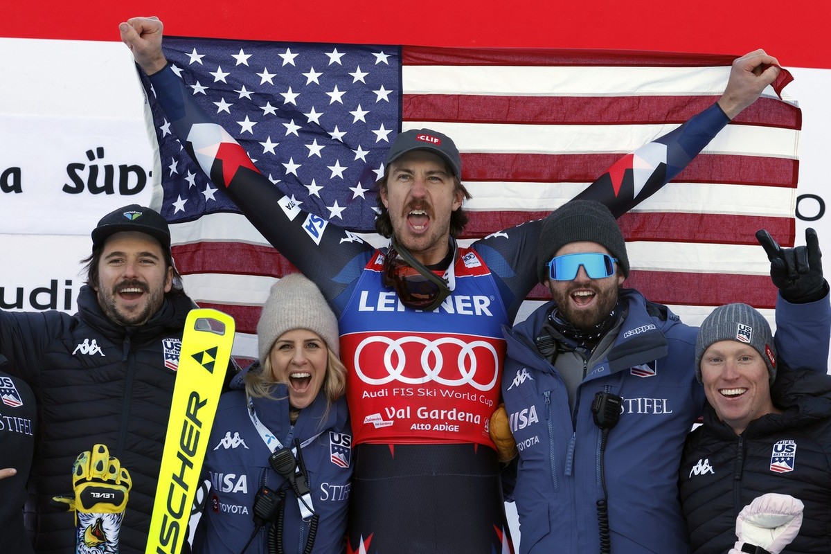 United States' Bryce Bennett, center, celebrates on the podium with the team after winning an alpine ski, men's World Cup downhill race, in Val Gardena, Italy, Thursday, Dec. 14, 2023. (AP P ...