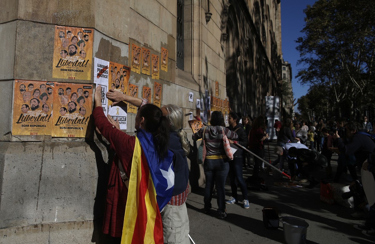 A woman with an 'Estelada', the pro-independence Catalan flag draped over her shoulder, pastes banners on a wall that read in Catalan: "Freedom for the Political Prisoners" during  ...