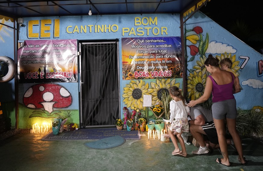A family stands at the door "Cantinho do Bom Pastor" daycare after a deadly attack on children in Blumenau, Brazil, Wednesday, April 5, 2023. A man with an ax jumped over a wall and ...