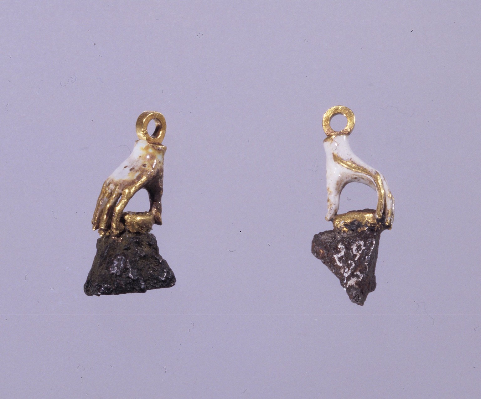 Ear ornaments in white gold enamel shaped as hands, holding splinters from a blown up cannon and a Swedish cannon ball that injured Christian IV in the naval battle of Kolberger Heide. The ornaments b ...