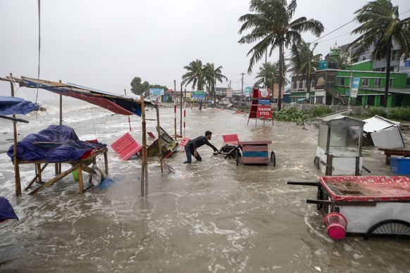 A man salvages a cart and other material as water flows on to the Kuakata beach on the coast of Bay of Bengal caused by the advancing Cyclone Remal in Barisal, Bangladesh, Sunday, May 26, 2024. (AP Ph ...