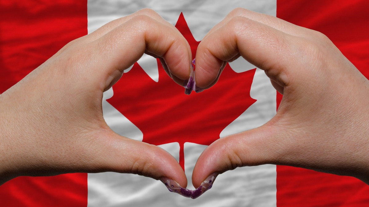 Gesture made by hands showing symbol of heart and love over national canada flag