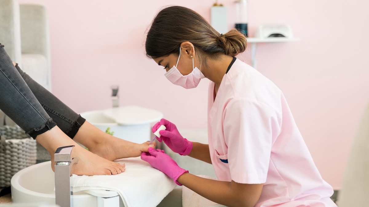 Female pedicurist applying nail polish on customer toenails at beauty salon