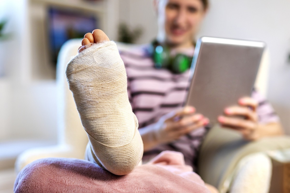 Close-up of young woman with leg in plaster using digital tablet at home. Close up of females leg in plaster. Human body part.