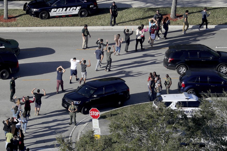FILE - In this Wednesday, Feb. 14, 2018 file photo, students from Marjory Stoneman Douglas High School in Parkland, Fla., hold their hands in the air as they are evacuated by police after a shooter op ...