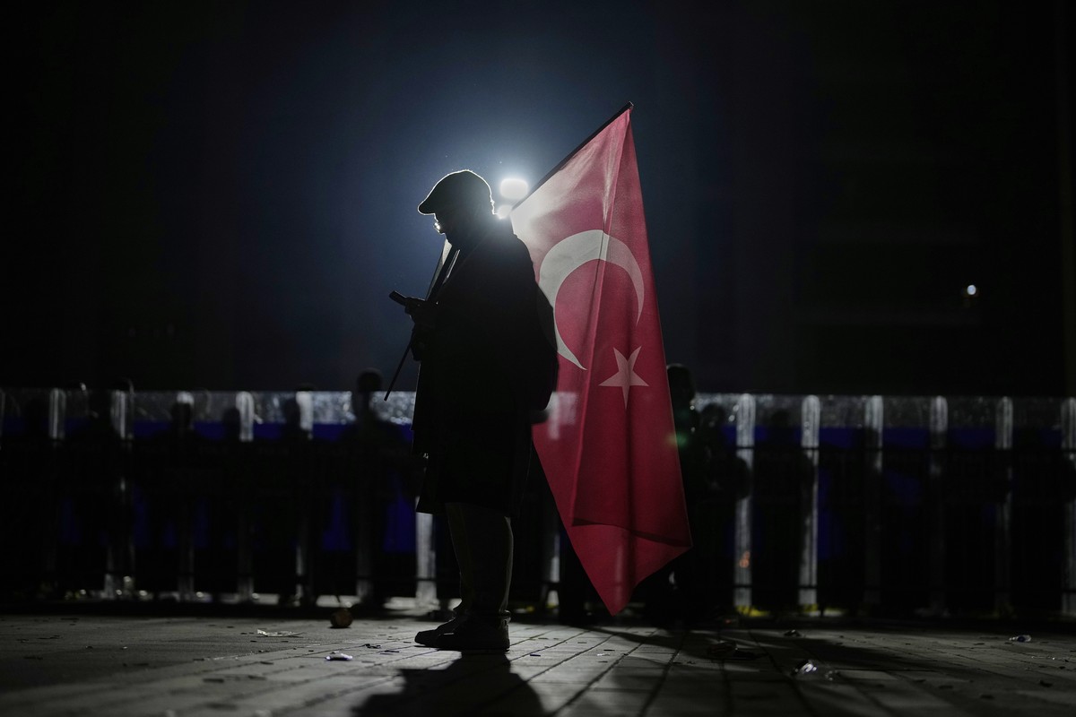 A protester holds a Turkish flag as riot police stand guard during a protest against the arrest of Istanbul's Mayor Ekrem Imamoglu, outside Caglayan courthouse, in Istanbul, Turkey, Sunday, March ...