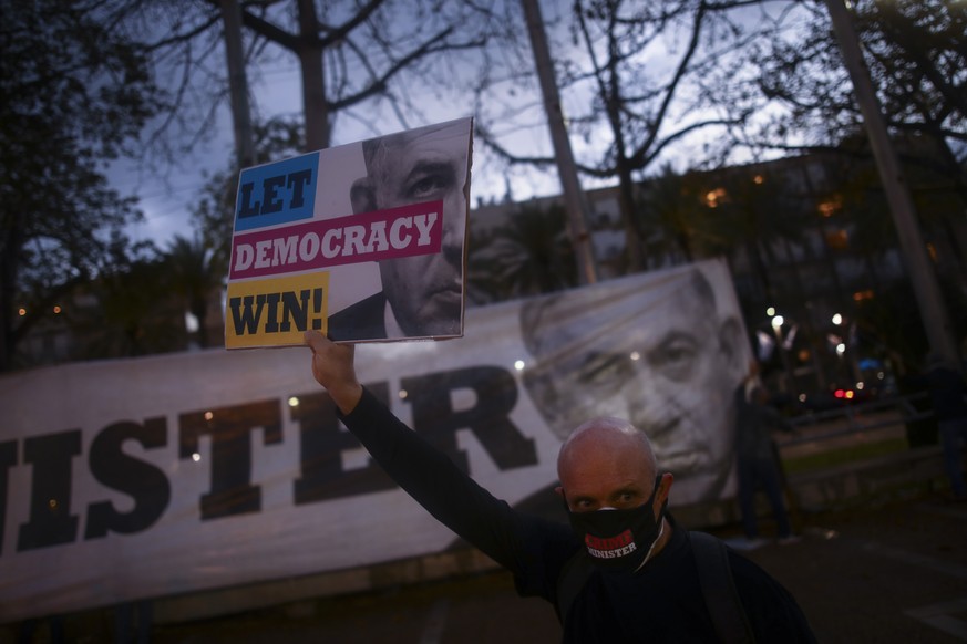 A man wears a protective face masks amid concerns over the country&#039;s coronavirus outbreak, and holds a sign during &quot;Black Flag&quot; protest against Prime Minister Benjamin Netanyahu and gov ...