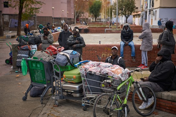 FILE - Migrants sit together with their belongings after being evicted by police from an abandoned school where they had been living in Badalona, near Barcelona, Spain, Wednesday, Dec. 17, 2025. (AP P ...
