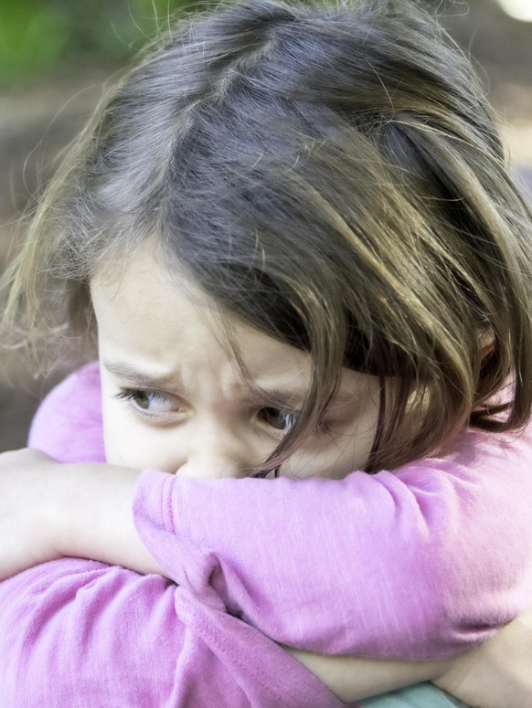 Sad crying little girl resting at a playground swing looking at the camera