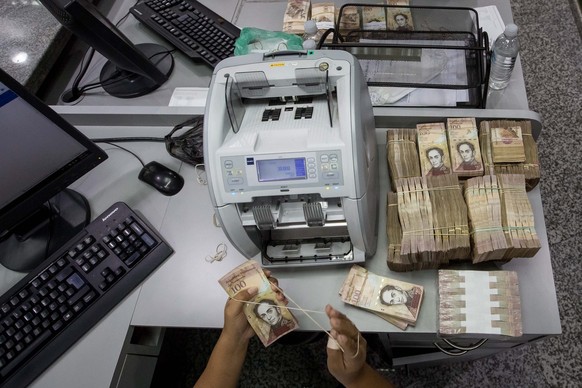 epa05677470 A bank worker counts 100 Bolivares bills in Caracas, Venezuela, 15 December 2016. Thousands of Venezuelans head to the banks to get rid of their 100 Bolivares bills, the highest denominati ...