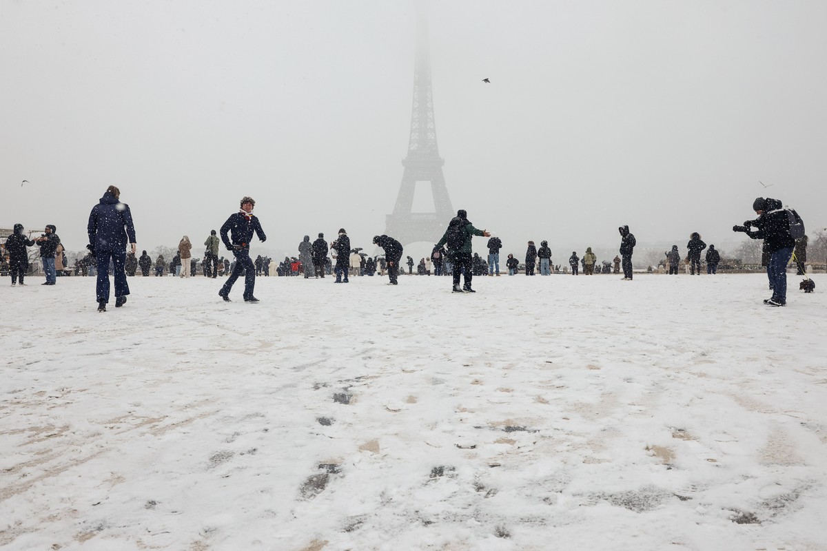 epa12629166 People walk during a snowfall near the Eiffel Tower in Paris, France, 05 January 2026. Meteo-France issued an orange alert for 26 departments, including the Paris region, as severe winter  ...