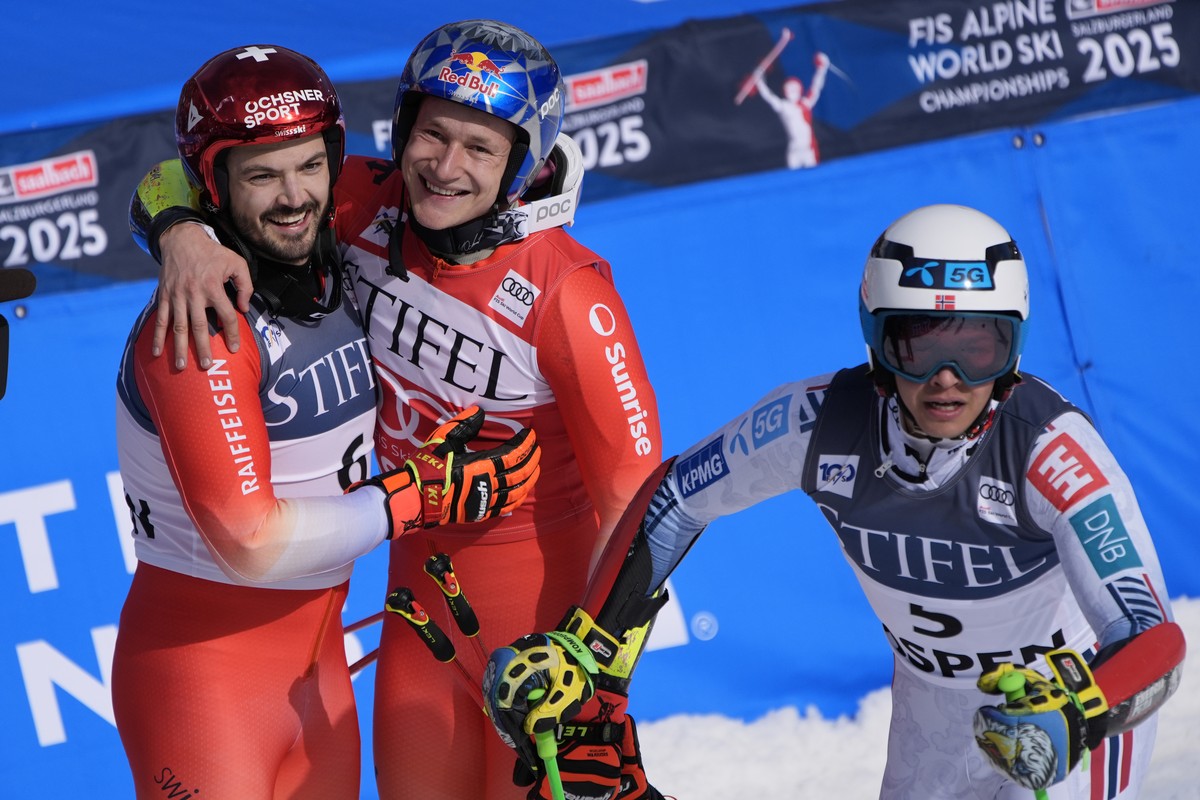 First place finisher Switzerland's Marco Odermatt, center, embraces second place finisher Switzerland's Loic Meillard after a men's World Cup giant slalom skiing race Saturday, March 2, ...