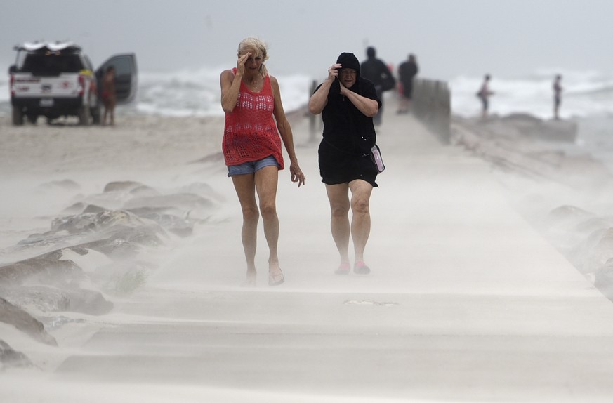 People shield their faces from wind and sand ahead of Tropical Storm Nicholas, Monday, Sept. 13, 2021, on the North Packery Channel Jetty in Corpus Christi, Texas. Lifeguards paroled the beach to warn ...