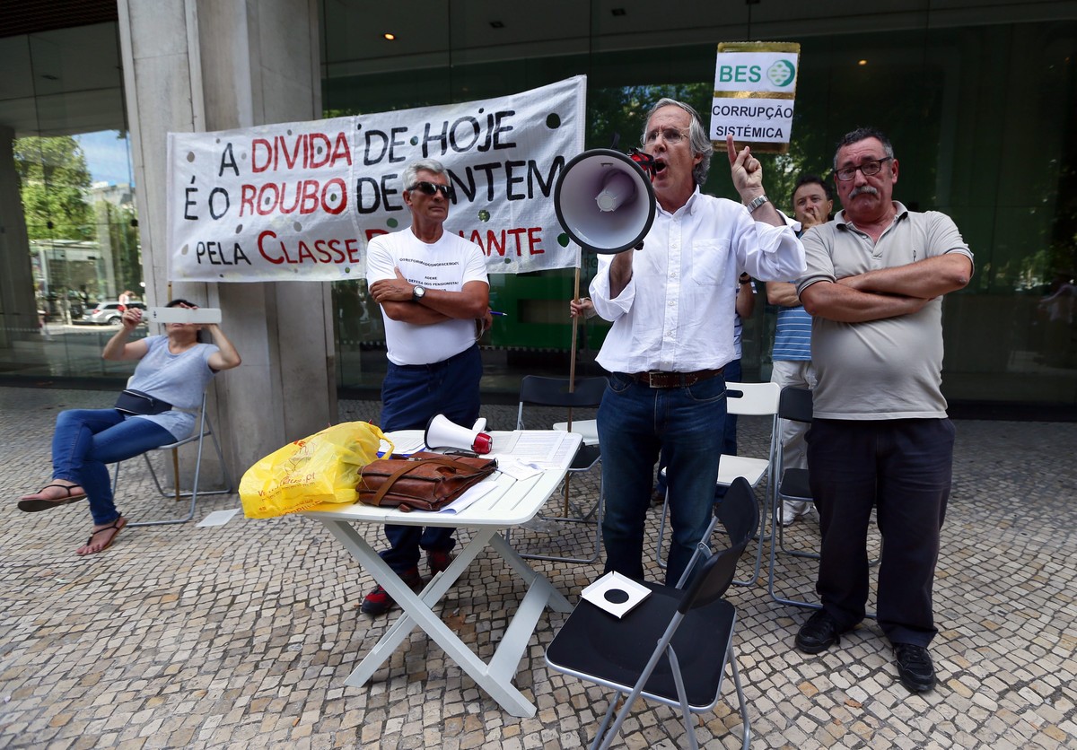 epa04347319 Protesters hold banners with the words 'Today's debt if the theft of yesterday made by the dominant class' (L) and 'BES - sistemic corruption', during a protest in ...
