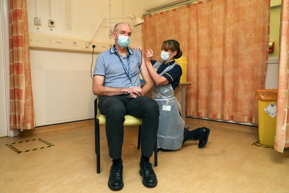 Professor Andrew Pollard, Director of the Oxford Vaccine Group, and a professor of paediatric infection and immunity receives the Oxford University/AstraZeneca COVID-19 vaccine from nurse Sam Foster a ...