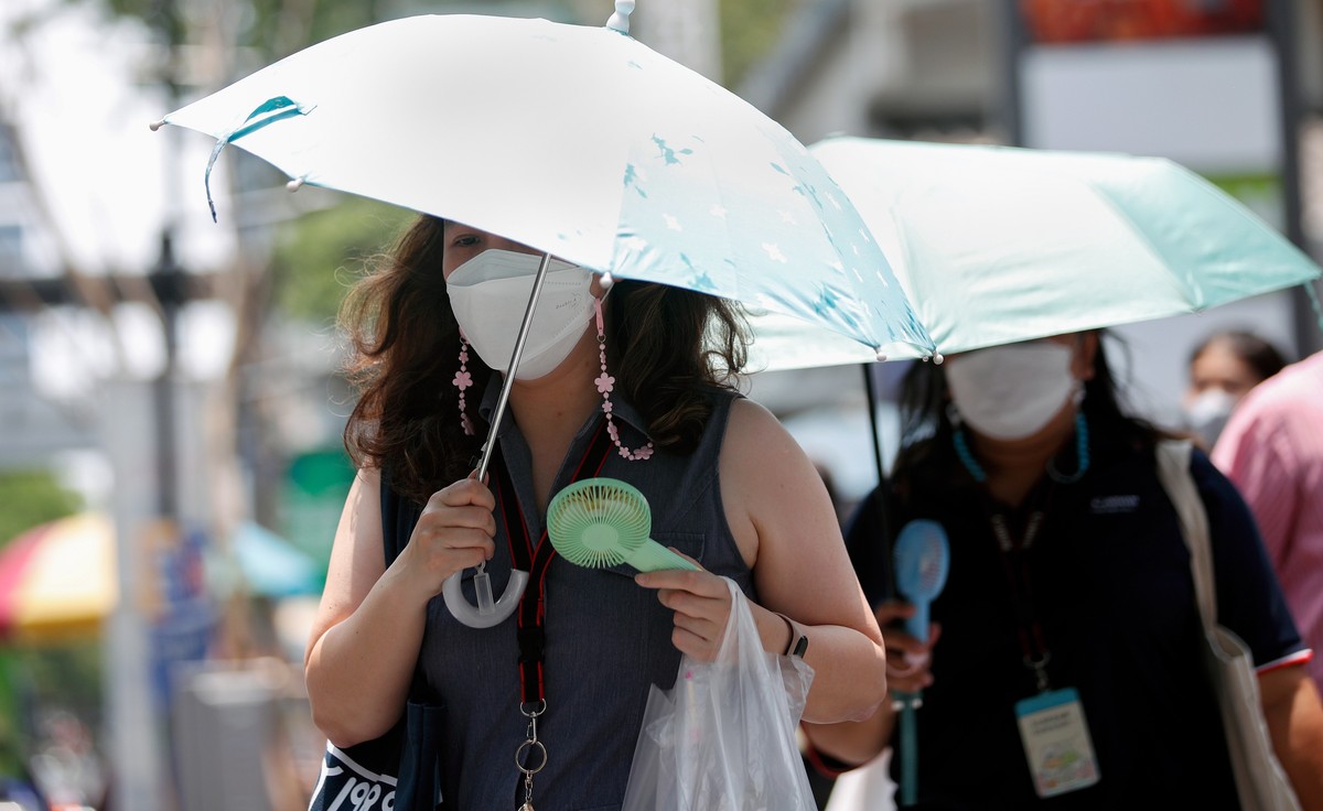 epa10596103 Office workers use umbrellas to shield sunlight and cool down with their electric handheld fans during hot weather in Bangkok, Thailand, 28 April 2023. Thailand experiences extreme heat wa ...
