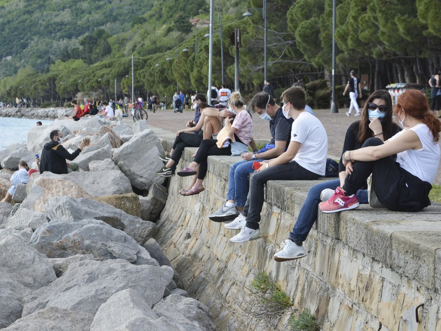 epa08398929 People in protective masks sit on a wall on the waterfront of the Adriatic Sea in Barcola, Italy, 03 May 2020. The Italian government announced a gradual lifting of the lockdown restrictio ...