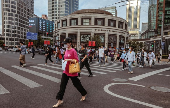 epa10213302 People walk next to the large screen showing latest stock and currency exchange data, in Shanghai, China, 29 September 2022. China&#039;s yuan hit a record low against the US dollar on 28  ...