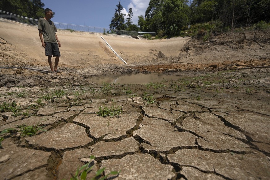 Gan Bingdong stands in the basin of a community reservoir near his farm that ran nearly empty after its retaining wall started to leak and hot weather and drought conditions accelerated the loss of wa ...