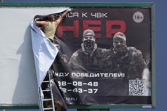 A man takes down a poster reading "Join Wagner"who is associated with the owner of the Wagner private military contractor, Yevgeny Prigozhin, is seen above a highway on the outskirts ...