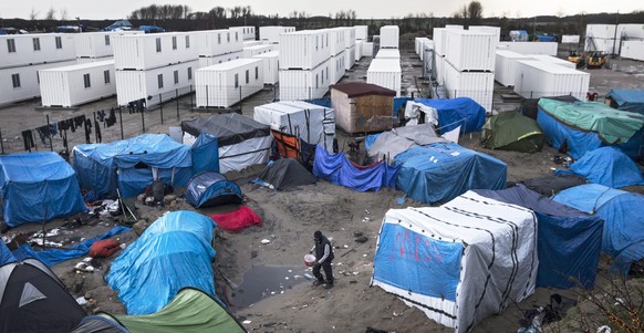 epa05095992 A migrant walks among the tents and huts of the makeshift camp called 'The Jungle' next to the fenced area made of containers recycled in rooms to host some 1,500 migrants in Calais, Franc ...