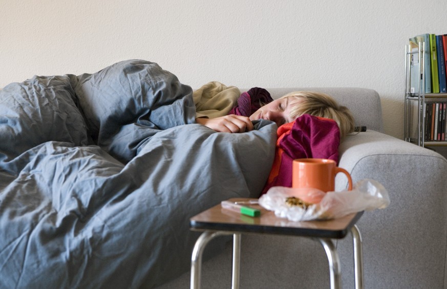 [Themenbild Grippe, gestellte Aufnahme] Eine Frau kuriert auf dem Sofa ihre Grippeerkrankung mit Schlaf aus, aufgenommen am 27. Oktober 2007 in Zuerich. Daneben auf einem Hocker sind eine Tasse Tee, B ...