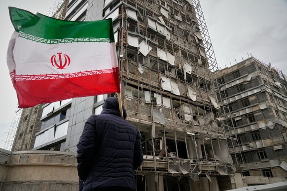 A man holds an Iranian flag as he looks at the damaged façade of Gandhi Hospital, which was hit Sunday when a strike also struck a state TV communications tower and nearby buildings across the street  ...