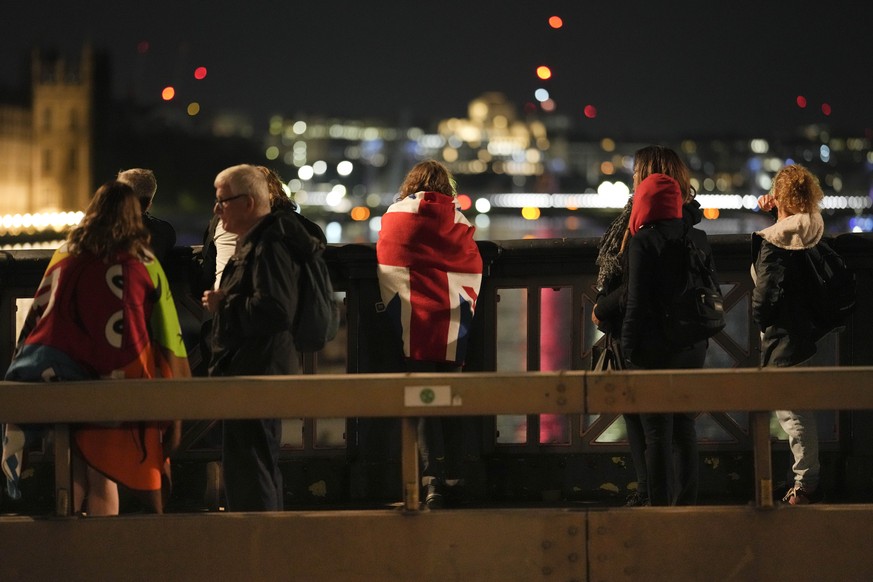 A woman draped with a Union flag waits with other people in the queue near Westminster Palace to pay their respect to the late Queen Elizabeth II during the Lying-in State, at Westminster Hall in Lond ...