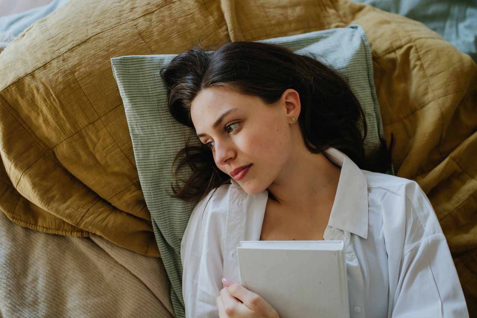 Top view of woman thinking about book in bed, cozy and contented feeling, finished story. Freedom in story, weekend activity for single woman. Top view of woman thinking about book in bed, cozy and co ...